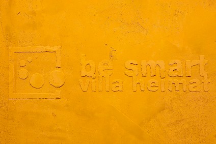 be smart villa Heimat logo als Relief an einer gelben Wand