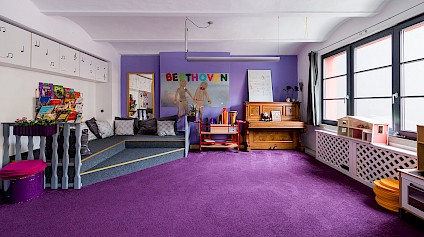 Die Musikecke im Beethoven-Raum mit flauschigem violetten Teppich, Trommeln, Klavier und weiteren Instrumenten
