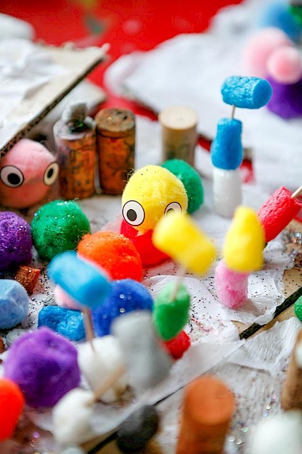 Kleine gebastelte Figuren aus bunten Stoffkugeln mit Kulleraugen